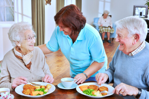 Elderly couple dining with caregiver assistance.
