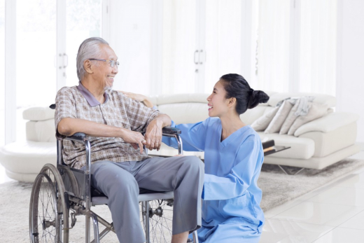 Elderly man in wheelchair with caregiver smiling.