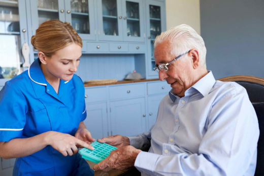 Nurse assisting elderly man with medication organizer.