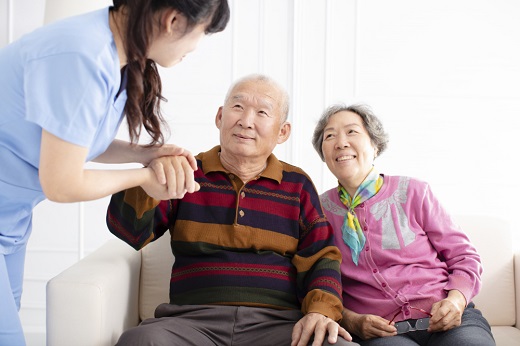 Caregiver assisting elderly couple on couch.