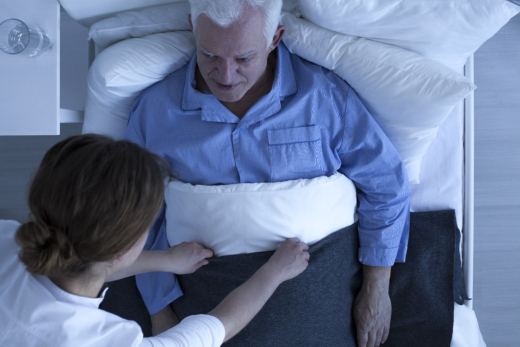 Elderly man in bed with caregiver assistance.