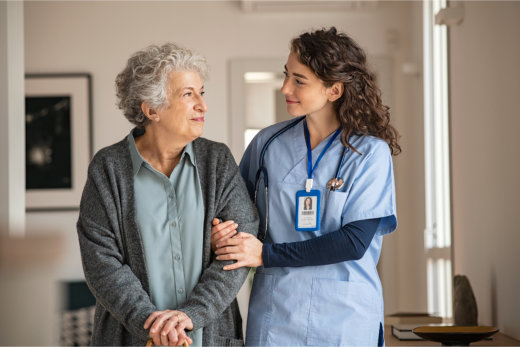 Nurse supporting elderly woman with cane.
