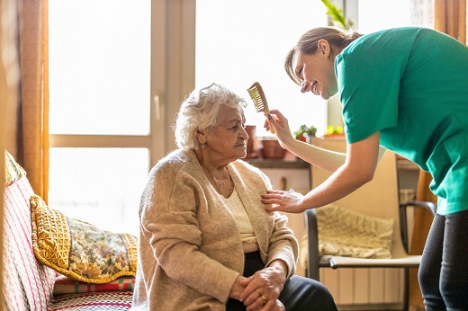 Caregiver brushing elderly woman's hair gently.