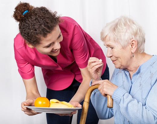 Caregiver offering fruit to elderly woman.