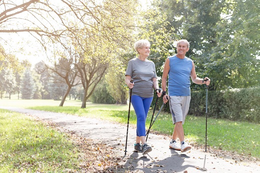 Elderly couple walking with trekking poles outdoors.