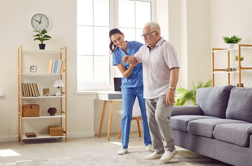 Nurse assisting elderly man in living room.