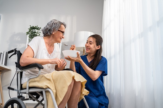 Caregiver feeding elderly woman in wheelchair.