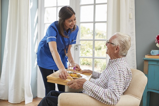 Caregiver serving meal to seated elderly man.