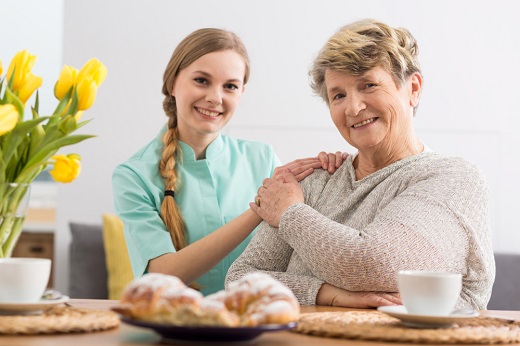 Caregiver and elderly woman smiling at table.