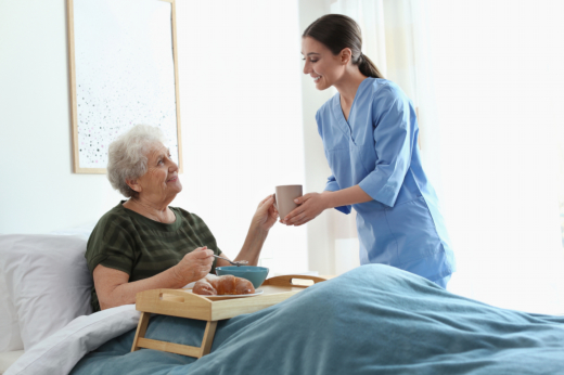 Caregiver serving breakfast to elderly woman.