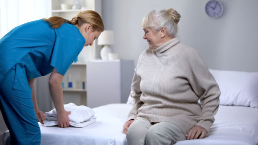 Nurse assisting elderly woman on bed.