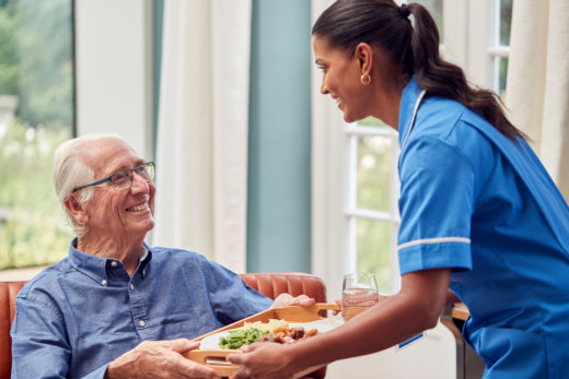 Caregiver serving meal to elderly man.
