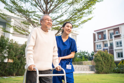Elderly man with caregiver outdoors, smiling.
