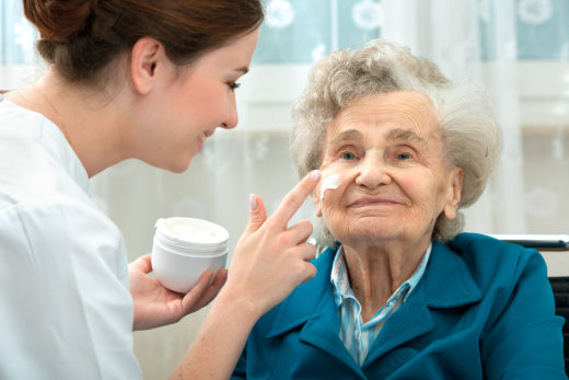 Caregiver applying cream to elderly woman's face.